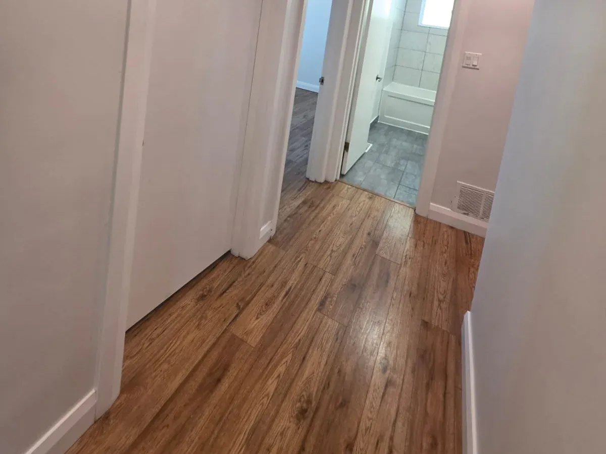 Hallway with new wood-look plank flooring running through white door casings toward a tiled bathroom