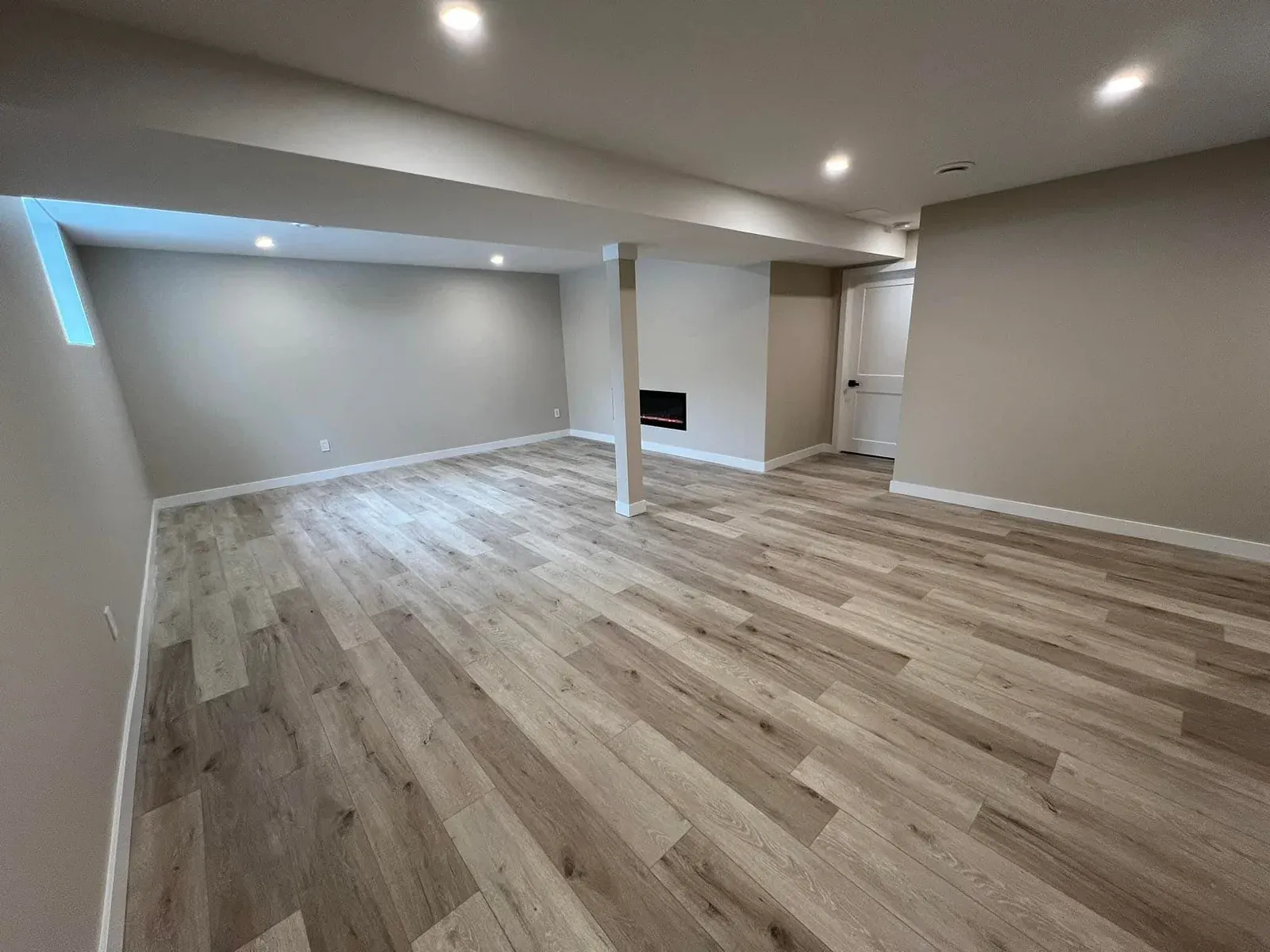 Finished basement family room with pot lights, white trim, and light wood-look plank flooring