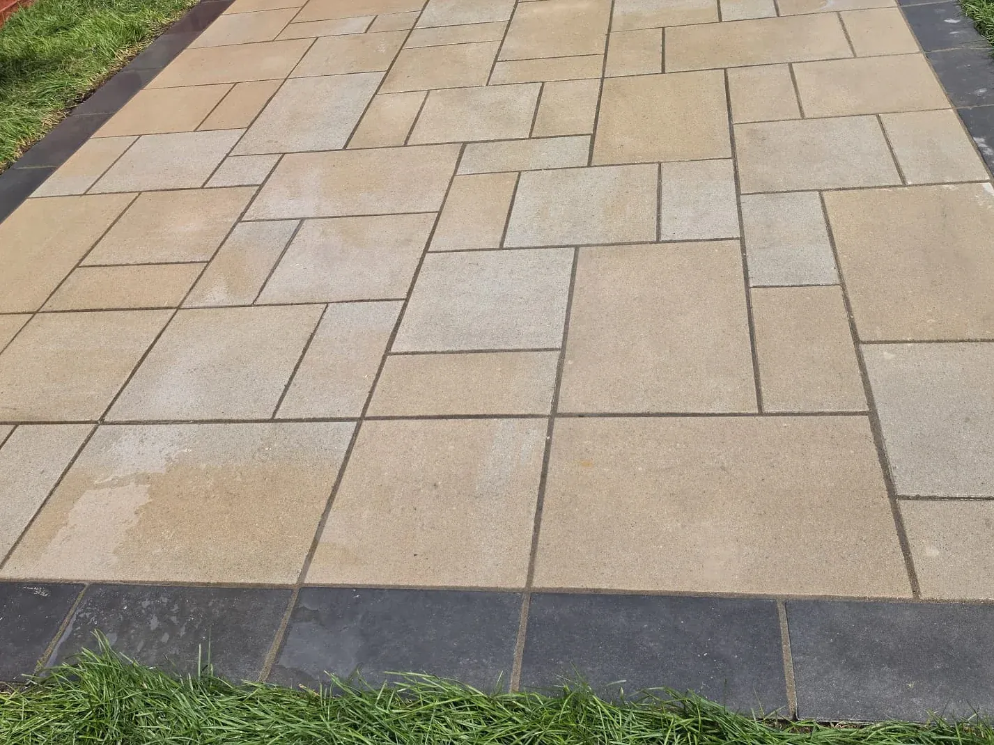 Backyard interlocking stone patio of tan pavers with a charcoal border, edged by fresh lawn